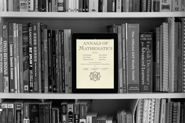 Tablet screen showing Annals of Mathematics journal on a book shelf with reference books.