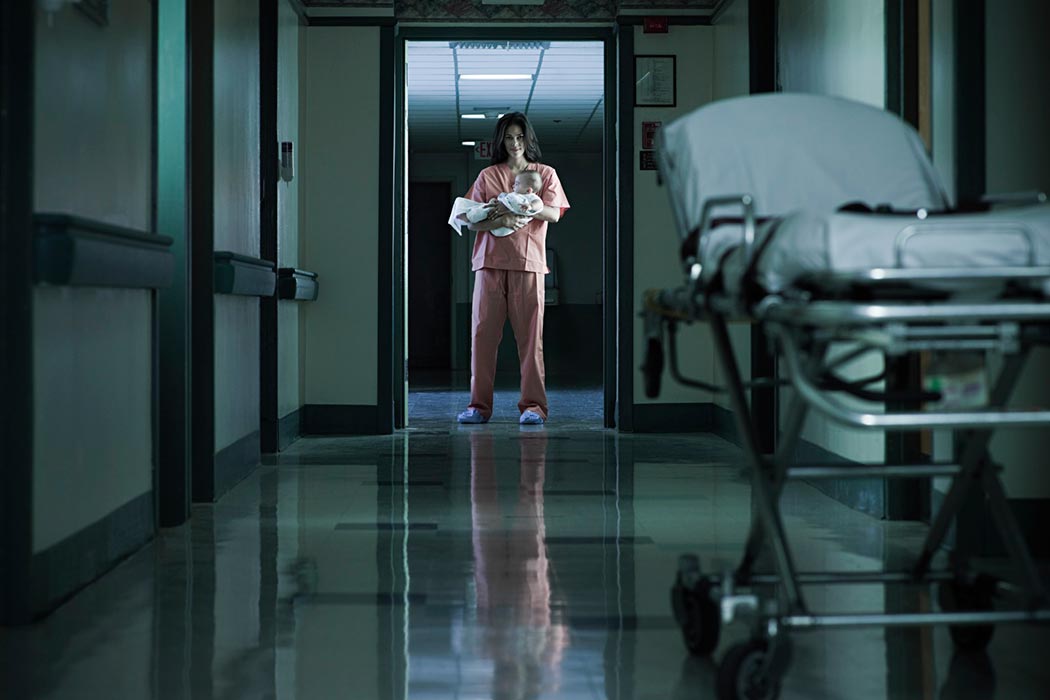 A maternity ward worker holds a baby in an empty hospital hall