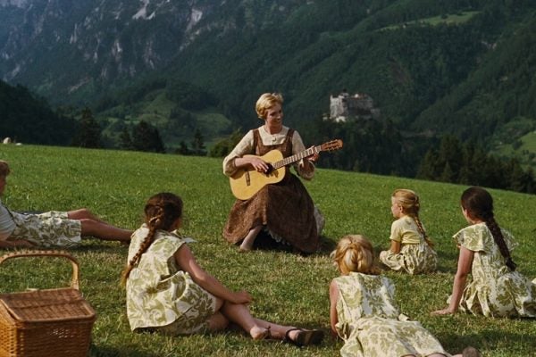 Still from The Sound of Music showing the von Trapp family sprawled out and circling a guitar-playing Maria