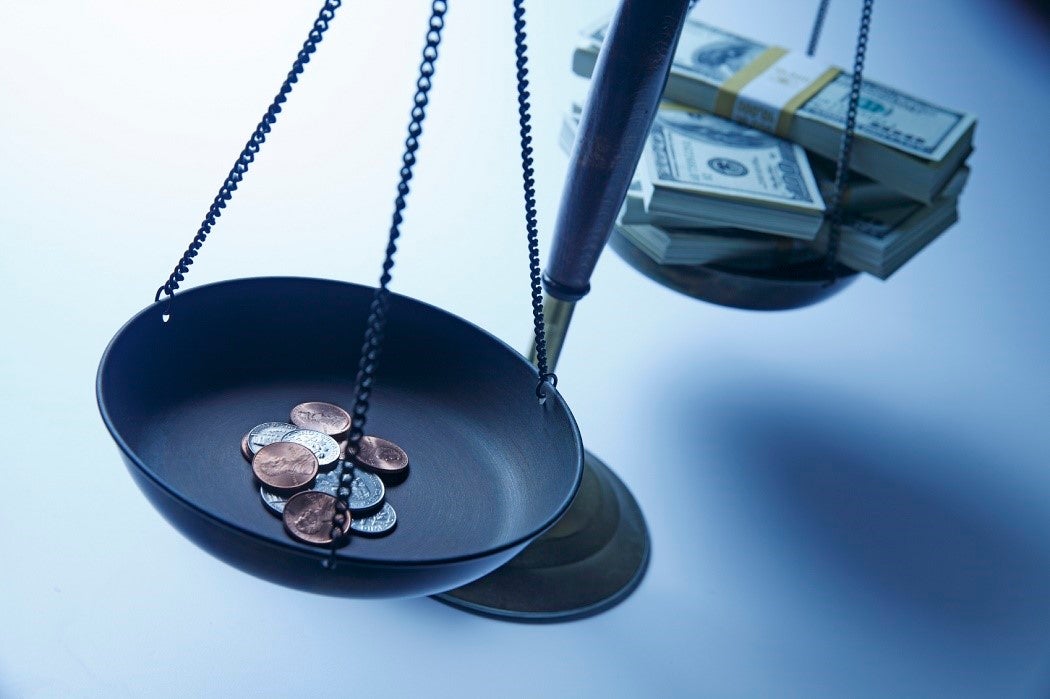 A scale with coins on one side and stacks of hundred dollar bills in the other; the scales are balanced.