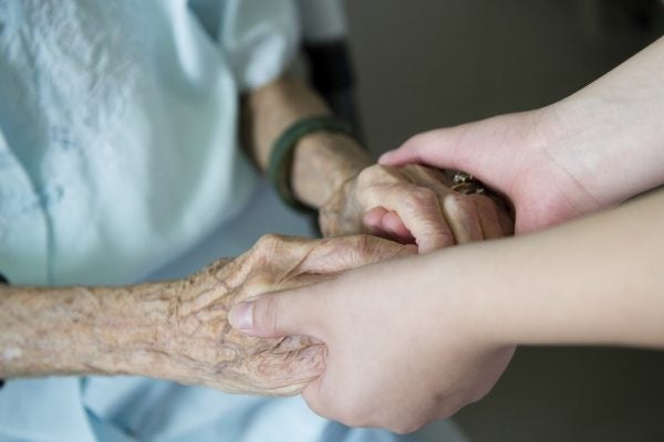 Young girl's hand touches and holds an old woman's wrinkled hands.