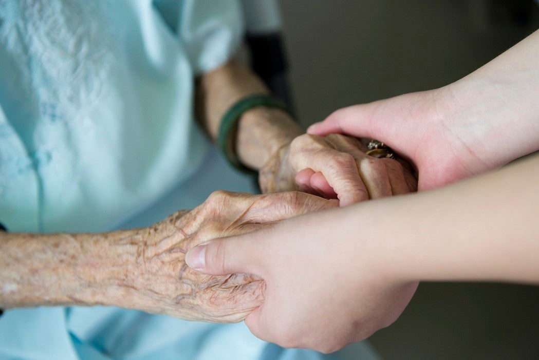 Young girl's hand touches and holds an old woman's wrinkled hands.