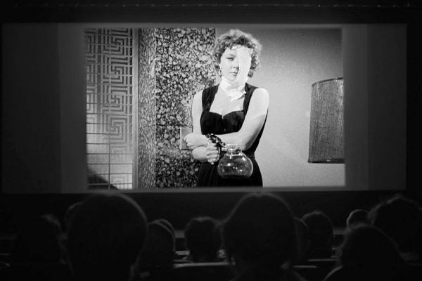 A movie audience watches 1950's actress Gloria Graham with bandages over one side of her face from an older film