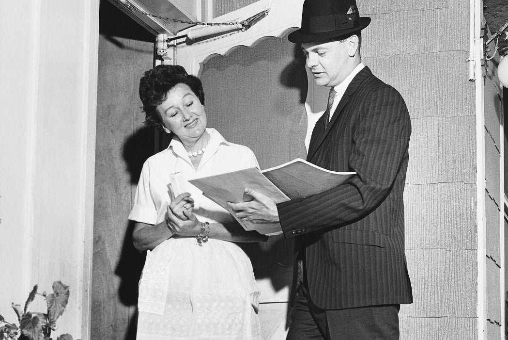 A black and white photograph of a 1590's housewife speaking to a salesman at her door