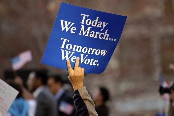 Protestor holding up a sign reading, "Today we march...tomorrow we vote."