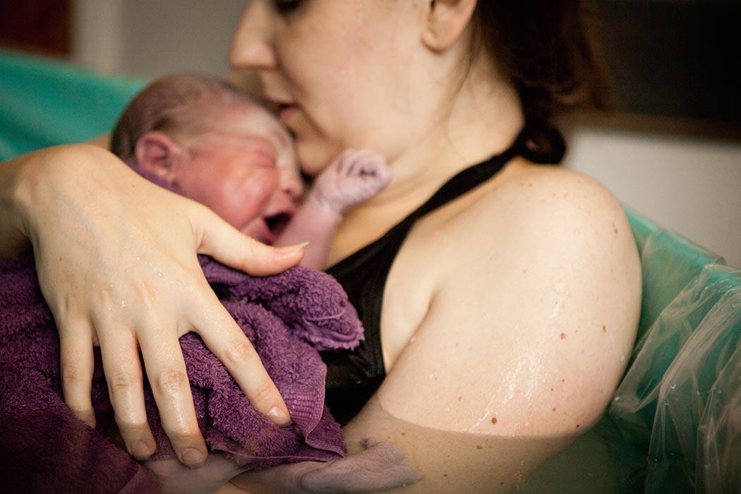 A mother holding her newborn in a birthing tub after her home water birth.