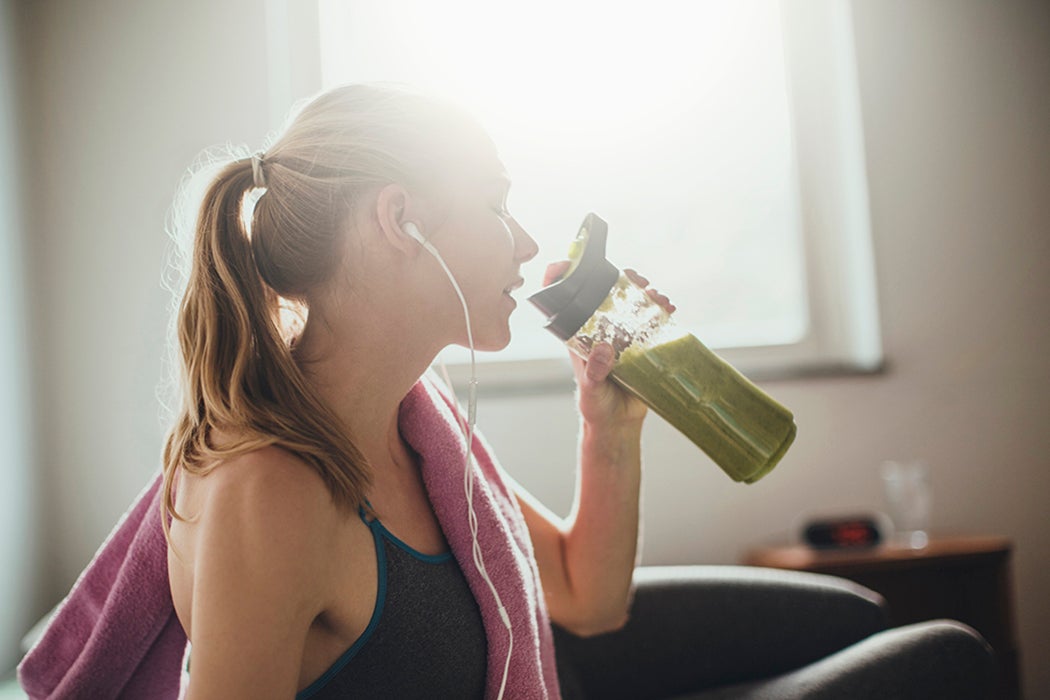 Young woman drinking a green smoothie after training