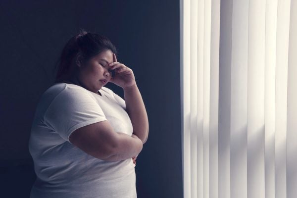 A woman in pain, standing beside a window