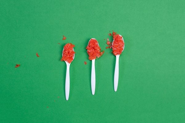 Three spoonfuls of red microplastic on a green background.