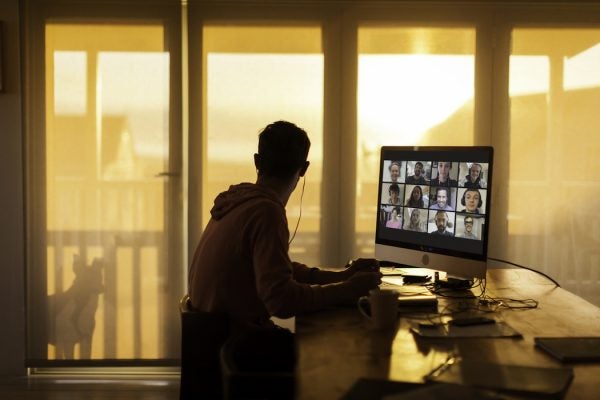 A young man looks out his balcony window, ignoring his Zoom call