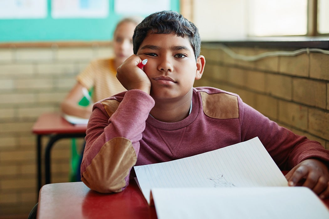 A young boy looking bored at his desk in a classroom