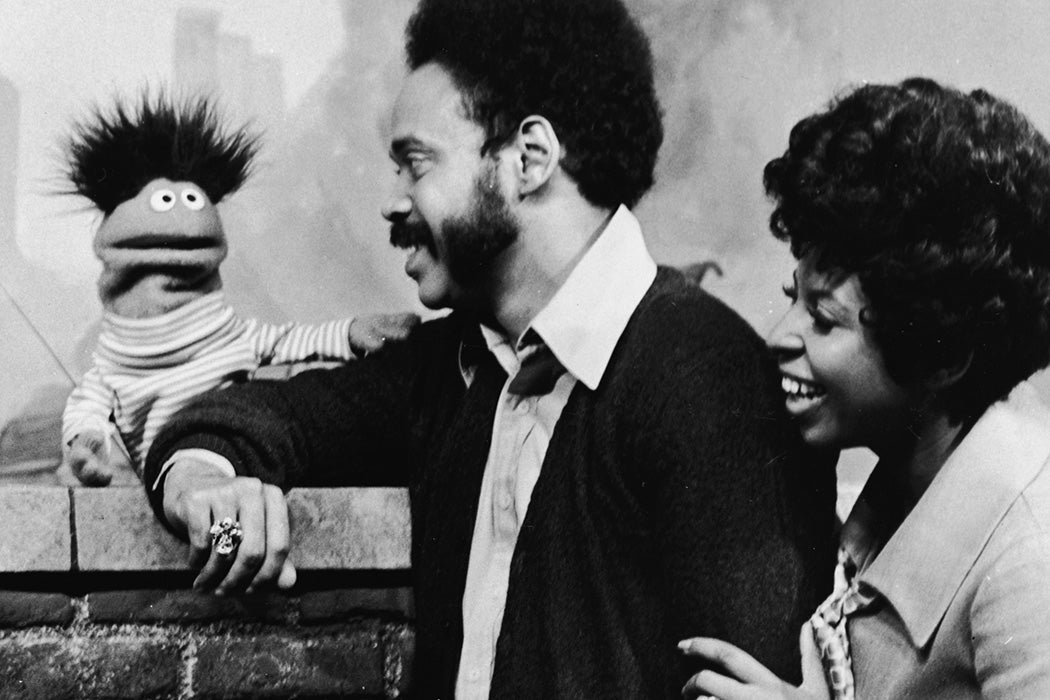 Matt Robinson (as Gordon) and Loretta Long (as Susan) lean on a brick wall and speak with Roosevelt Franklin, 1970