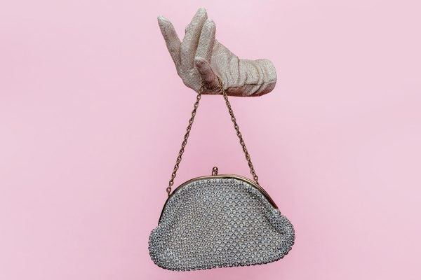 Studio photograph of Floating gloved hand holding purse on pink background.