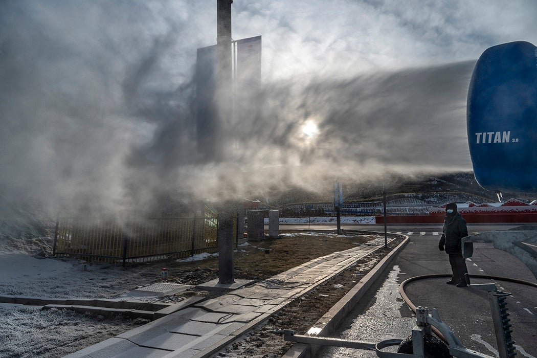 A worker stands next to a snow machine making artificial snow outside one of the athletes villages for the Beijing 2022 Winter Olympics before the area closed to visitors, on January 2, 2022 in Chongli county, Zhangjiakou, Hebei province, northern China.