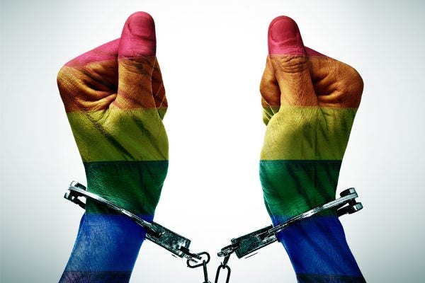 closeup of the hancduffed hands of a person patterned as the gay pride flag