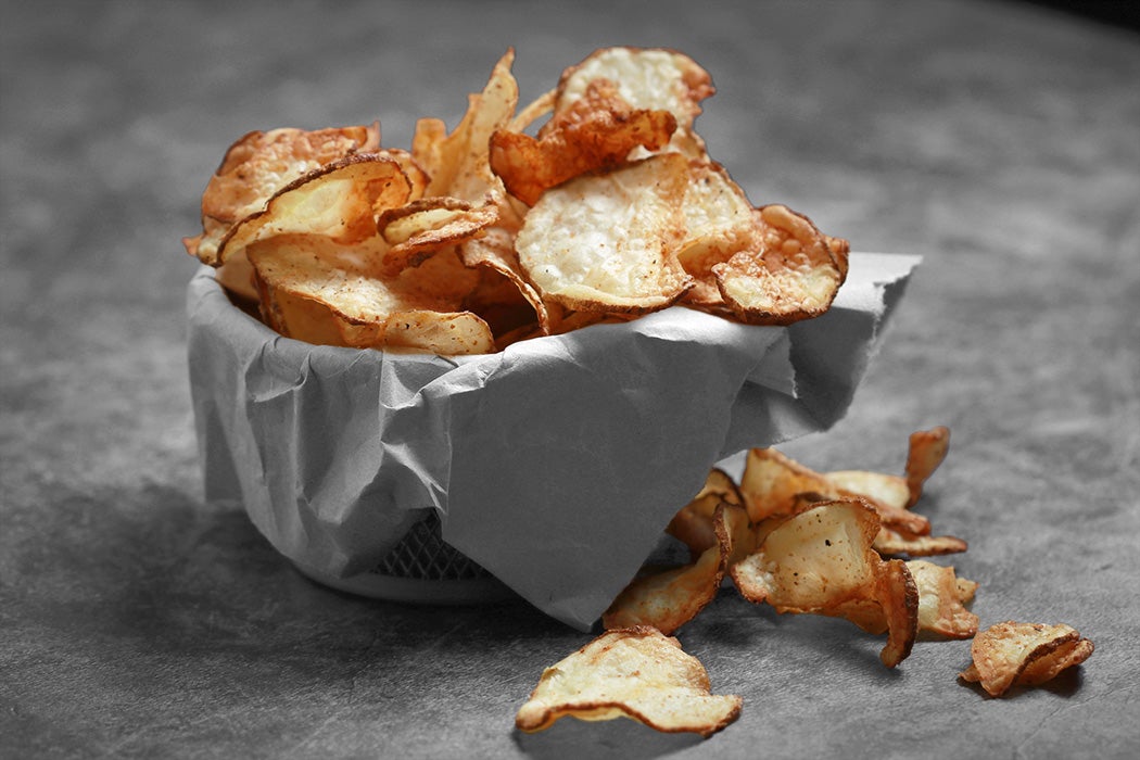 Homemade Air Fryer potato chips in a paper lined wire basket on dark background