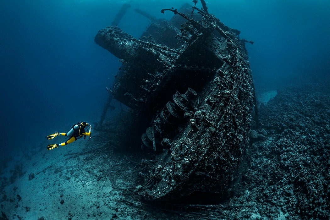 Scuba diver passing by a wreckage of a large sunken ship in the Red Sea.