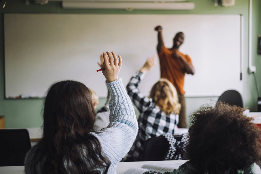 Rear view of girl raising hand while sitting with students in classroom