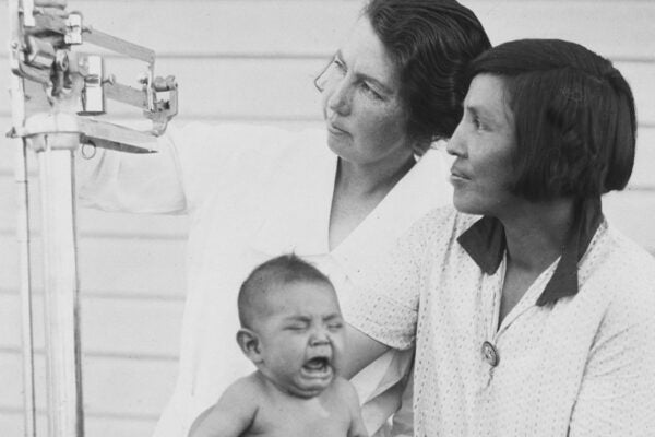 Native American midwives weighing a crying Native Amerian child on a set of scales in the hospital at the Glacier National Park, in northwestern Montana, on the Canada–United States border, circa 1945