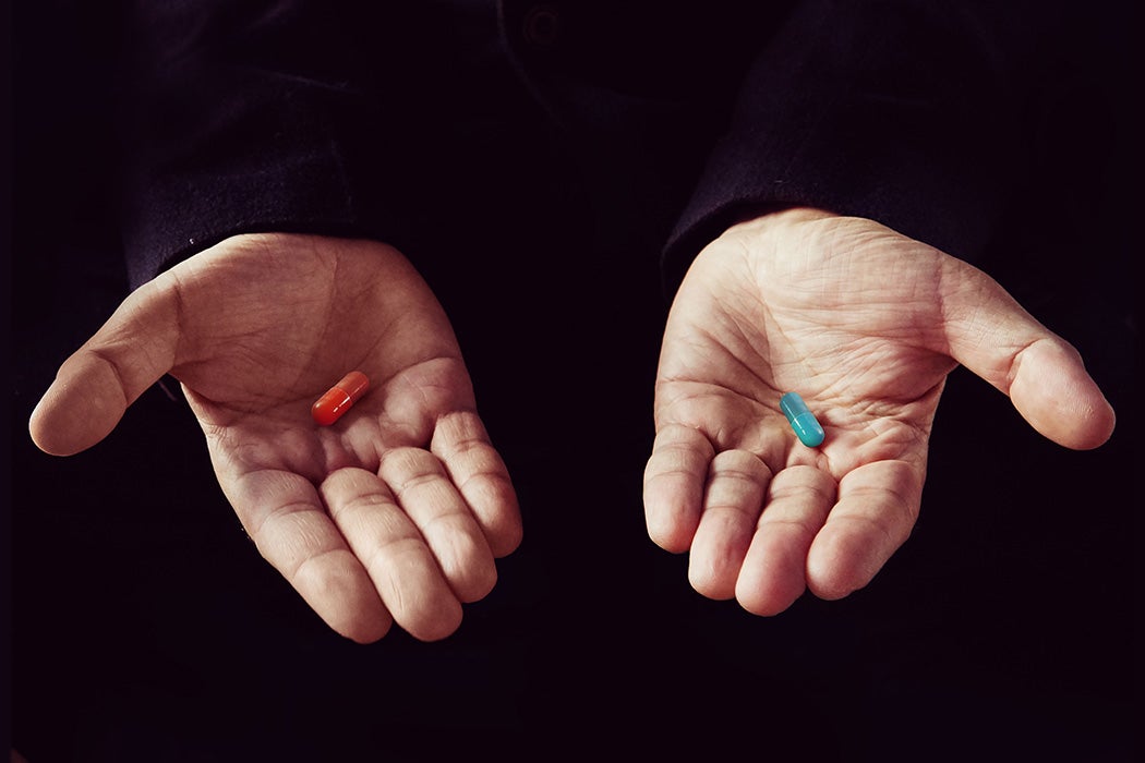 A photograph of a red pill in someone's left palm and a blue pill in his right palm