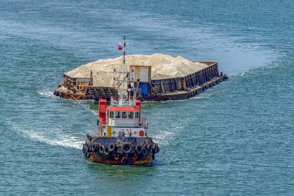 A tug boat towing a barge with sand in coastal waterway near Singapore